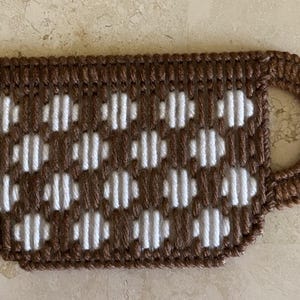 Pu&ograve; includere: Una tazza all'uncinetto marrone e bianca con un motivo a pois bianchi. La tazza ha un manico ed &egrave; realizzata in filato.