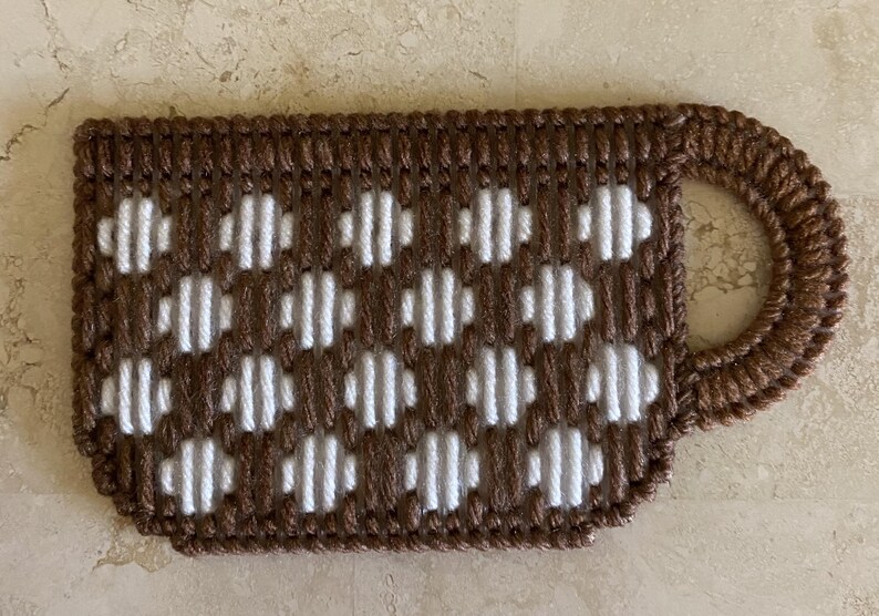 Pu&ograve; includere: Una tazza all'uncinetto marrone e bianca con un motivo a pois bianchi. La tazza ha un manico ed &egrave; realizzata in filato.