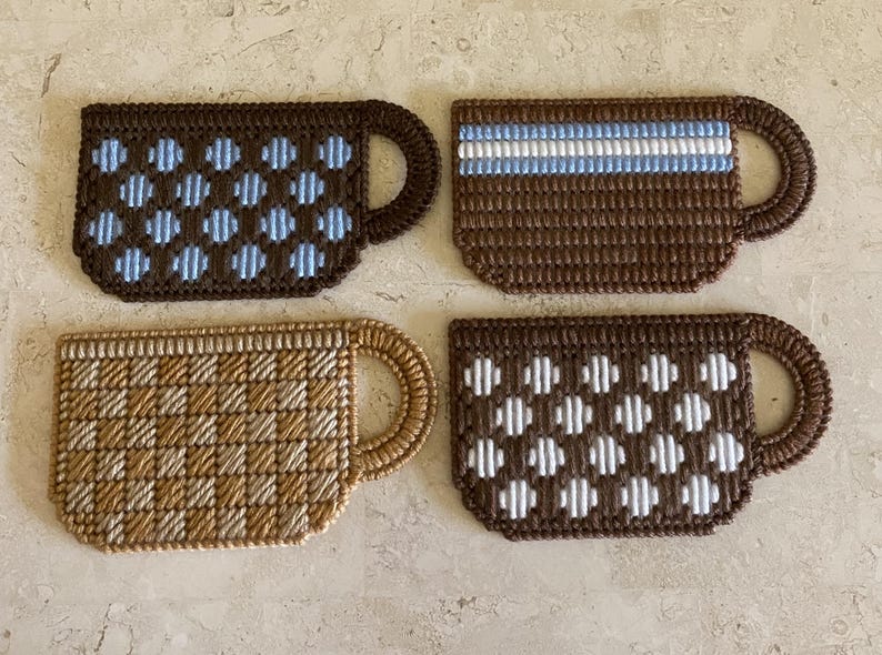 Pu&ograve; includere: Quattro sottobicchieri da caff&egrave; in crochet marroni con diversi motivi. I sottobicchieri presentano pois blu e bianchi, un motivo a scacchi marroni e bianchi, una striscia bianca e pois bianchi.