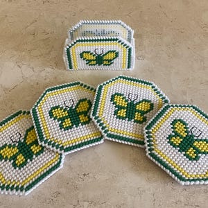 Puede incluir: Conjunto de cinco posavasos de ganchillo de color verde, blanco y amarillo con un diseño de mariposa. Los posavasos son hexagonales y tienen un borde elevado. También hay un portavasos de ganchillo a juego.