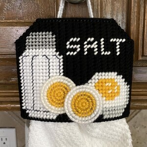 Puede incluir: Toallero de cocina de lona de plástico en blanco y negro con la palabra «SALT» e imágenes de un salero y huevos. Una toalla blanca cuelga del soporte. El soporte cuelga de un pomo plateado.