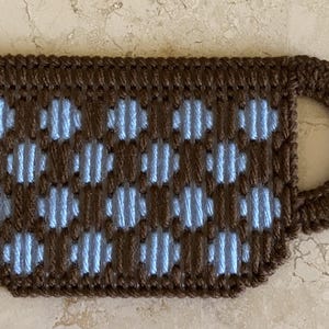 Pu&ograve; includere: Un sottobicchiere per tazza in crochet marrone e blu con un motivo a pois.