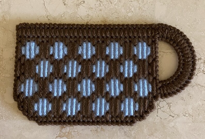 Pu&ograve; includere: Un sottobicchiere per tazza in crochet marrone e blu con un motivo a pois.