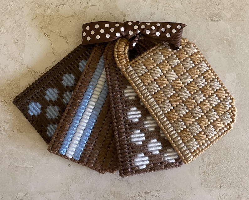 Pu&ograve; includere: Cinque etichette all'uncinetto marroni e bianche con diversi motivi, legate insieme con un nastro marrone e bianco a pois.