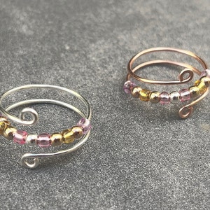 May include: Two delicate rings with a double wire design, adorned with small pink, gold, and silver beads.