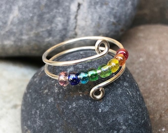 May include: A silver wire ring with a rainbow of small glass beads. The ring is on a gray rock.