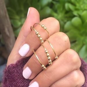 May include: Three gold rings with small beads on a finger. The rings are stacked on top of each other.