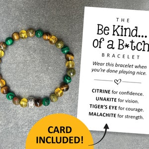 May include: A bracelet made with green, yellow, and brown beads with a silver charm. The bracelet comes with a card that reads "The Be Kind... of a B*tch Bracelet. Wear this bracelet when you're done playing nice. Citrine for confidence. Unakite for vision. Tiger's Eye for courage. Malachite for strength."