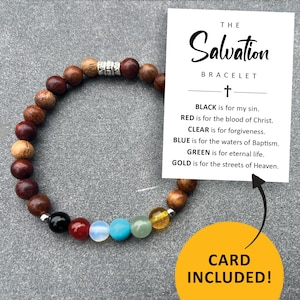 May include: The Salvation Bracelet is a wooden beaded bracelet with a silver charm. The bracelet features black, red, clear, blue, green, and gold beads. A card is included with the bracelet that explains the meaning of each color. The card reads: "The Salvation Bracelet. BLACK is for my sin. RED is for the blood of Christ. CLEAR is for forgiveness. BLUE is for the waters of Baptism. GREEN is for eternal life. GOLD is for the streets of Heaven. CARD INCLUDED!"