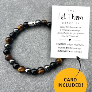 May include: A bracelet made with black onyx, tiger's eye, and hematite beads. The bracelet comes with a card that reads "THE Let Them BRACELET Wear this bracelet as a reminder to accept yourself and let go of what you can't control. HEMATITE to fight negativity. TIGER'S EYE for courage. BLACK ONYX for strength. CARD INCLUDED!"