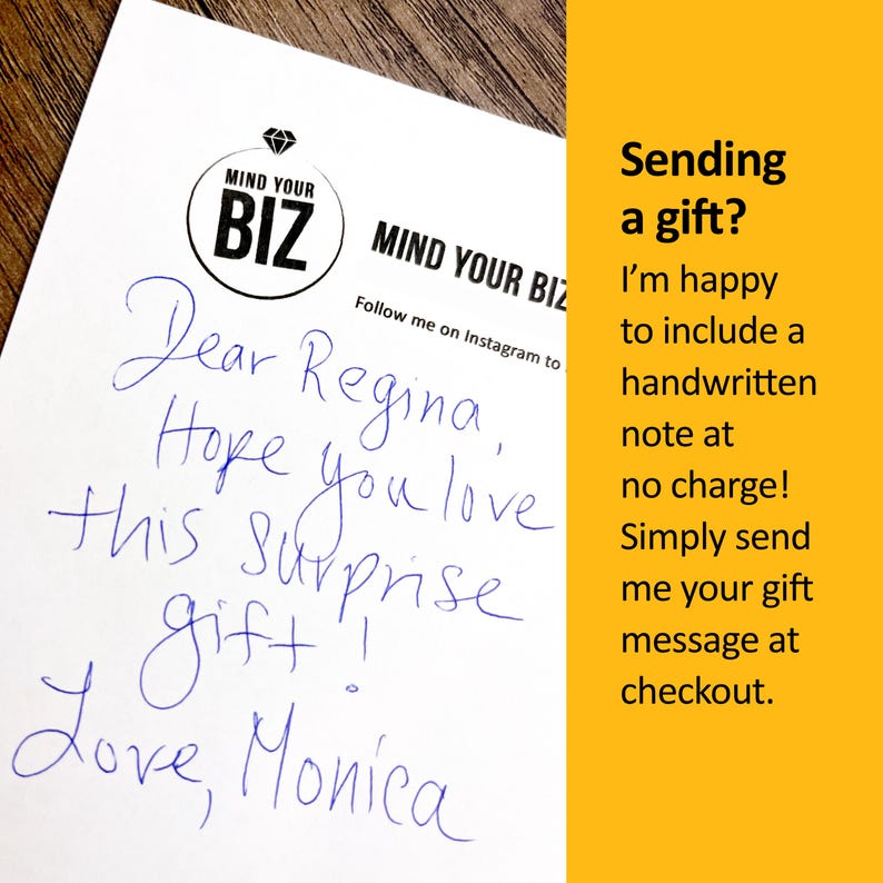 以下が含まれることがあります： 白い紙に青いインクで手書きされたメモ。メモはRegina宛で、Monicaのサイン入り。「MIND YOUR BIZ」のロゴが入っています。画像の右側にある黄色の背景には、ギフトノートに関するテキストがあります。