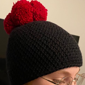 Könnte beinhalten: Schwarze Strickmütze mit einem großen roten Bommel oben.
