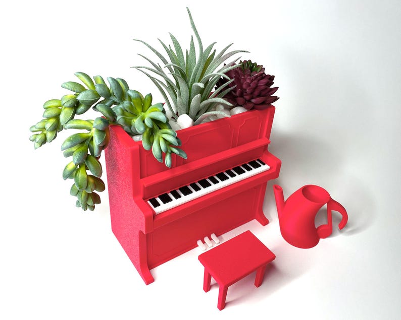 May include: A red piano-shaped planter filled with succulents and small white stones. A matching red stool, piano keys, and a musical note-shaped watering can are also present. The planter is a unique decorative item.