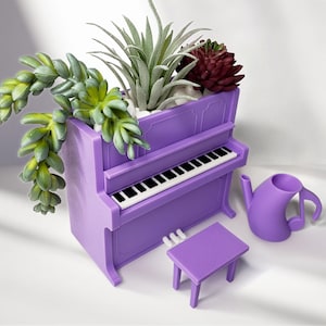 Może przedstawiać: Fioletowa donica w kształcie pianina z czarno-białą klawiaturą, zawierająca różne sukulenty i rośliny. Obok donicy znajduje się pasujący fioletowy stołek i konewka w kształcie nuty. Rośliny obejmują zielone i czerwone sukulenty.