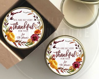 May include: Two round candle jars with gold lids and labels. The labels feature a watercolor design of fall leaves, flowers, and pumpkins. The text on the labels reads "We are so very thankful for you! Love the Johnsen's".