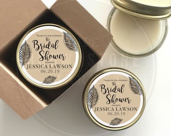 May include: Two gold candle jars with white labels. The labels have black text that reads "Thank you for attending The Bridal Shower Honoring Jessica Lawson 06.20.19". The labels also have black and white leaf designs.