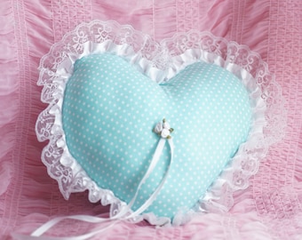 May include: A heart-shaped pillow with a light blue polka dot fabric and white lace trim. The pillow has a white satin ribbon and a small white flower embellishment.