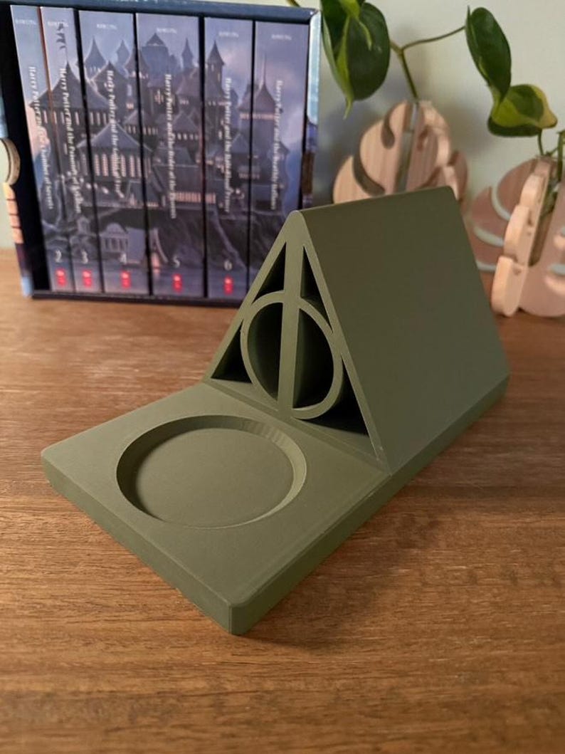 K&ouml;nnte beinhalten: Ein gr&uuml;ner, 3D-gedruckter Harry-Potter-Telefonst&auml;nder mit einem Symbol der Heiligt&uuml;mer des Todes und einer runden Vertiefung f&uuml;r ein Telefon.
