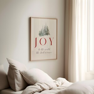 K&ouml;nnte beinhalten: Ein gerahmter Druck mit dem Wort "JOY" in Rot, &uuml;ber dem Satz "to the world, the Lord is come!" in einer Schreibschrift. Das Bild enth&auml;lt eine Aquarellillustration von immergr&uuml;nen B&auml;umen. Der Rahmen hat eine helle Holzfarbe.