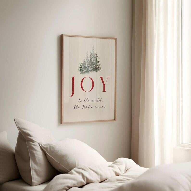 K&ouml;nnte beinhalten: Ein gerahmter Druck mit dem Wort "JOY" in Rot, &uuml;ber dem Satz "to the world, the Lord is come!" in einer Schreibschrift. Das Bild enth&auml;lt eine Aquarellillustration von immergr&uuml;nen B&auml;umen. Der Rahmen hat eine helle Holzfarbe.
