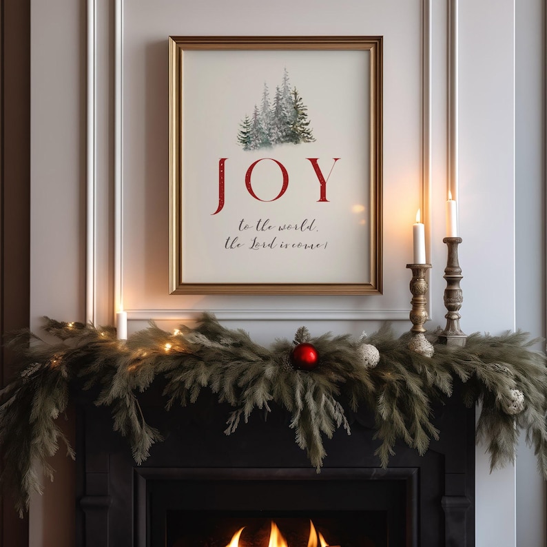 K&ouml;nnte beinhalten: Gerahmter Druck mit dem Wort "JOY" in Rot, &uuml;ber dem Text "to the world, the Lord is come". Der Druck zeigt ein Aquarellbild von Nadelb&auml;umen. Der Rahmen ist goldfarben, und der Druck wird &uuml;ber einem Kamin mit Girlanden und Kerzen pr&auml;sentiert.