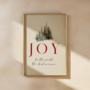 K&ouml;nnte beinhalten: Gerahmter Kunstdruck mit goldenem Rahmen. Der Druck zeigt eine Aquarellillustration von immergr&uuml;nen B&auml;umen &uuml;ber dem roten Wort "JOY". Darunter steht der Text "to the world, the Lord is come!"