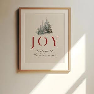 K&ouml;nnte beinhalten: Gerahmter Kunstdruck mit dem Wort "JOY" in Rot, &uuml;ber einem Aquarellbild von immergr&uuml;nen B&auml;umen. Der Satz "to the world, the Lord is come!" steht darunter in einer Schreibschrift. Das Kunstwerk befindet sich in einem hellen Holzrahmen.