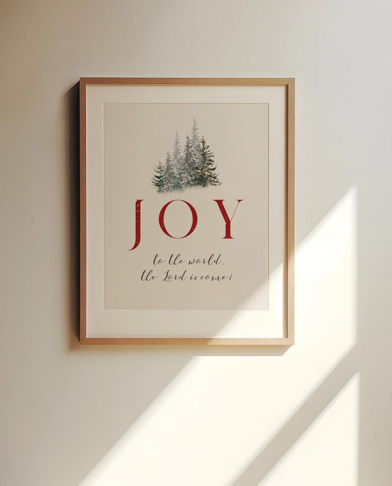 K&ouml;nnte beinhalten: Gerahmter Kunstdruck mit dem Wort "JOY" in Rot, &uuml;ber einem Aquarellbild von immergr&uuml;nen B&auml;umen. Der Satz "to the world, the Lord is come!" steht darunter in einer Schreibschrift. Das Kunstwerk befindet sich in einem hellen Holzrahmen.