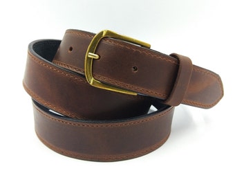 Op de afbeelding: Een bruine leren riem met een messing gesp. De riem is dubbelgevouwen en de gesp is zichtbaar.