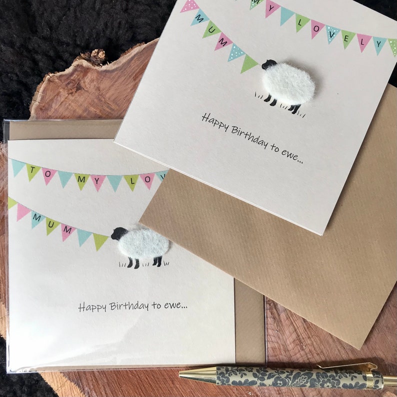 May include: Two greeting cards with a sheep design and the text "Happy Birthday to ewe...". The cards have a banner that says "MUMMY LOVELY" and "TO MY LOVE MUM". A pen with a floral design is also visible.