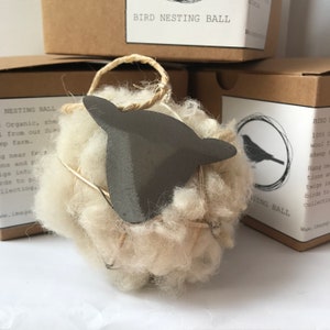 Op de afbeelding: Een witte wollen vogelnestbal met een metalen schapenkop. De bal is gemaakt van 100% biologische schapenwol en is ontworpen om buiten te worden opgehangen zodat vogels nestmateriaal kunnen verzamelen.