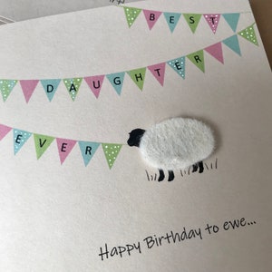 May include: A greeting card with a sheep illustration and the text "Happy Birthday to ewe...". The card features a banner that reads "Best Daughter Ever" in pink, green, and blue pennants.