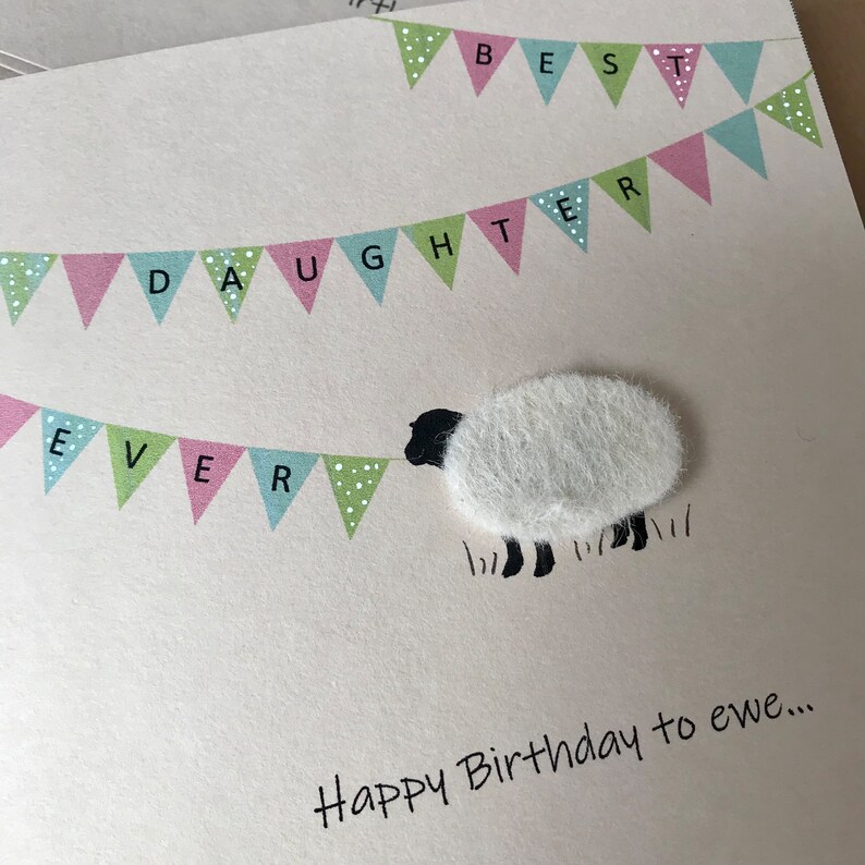 May include: A greeting card with a sheep illustration and the text "Happy Birthday to ewe...". The card features a banner that reads "Best Daughter Ever" in pink, green, and blue pennants.