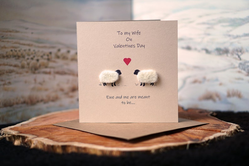 May include: A Valentine's Day card with a brown background and two white sheep with black faces. The card says "To my wife on Valentine's Day" and "Ewe and me are meant to be..." with a red heart between the sheep.