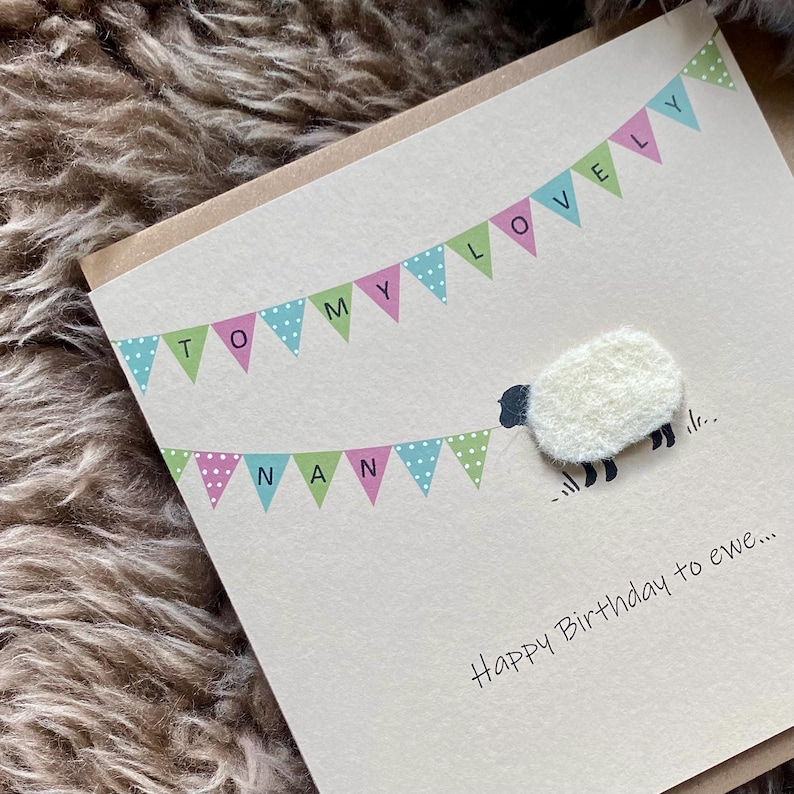 May include: A handmade greeting card with a cream-colored background. The card features a banner with the words "TO MY LOVELY NAN" and a fluffy white sheep. The text "Happy Birthday to ewe..." is written below the sheep.