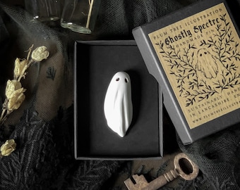 May include: A white ceramic ghost pin in a black box with a brown paper label that reads "Plum Tree Illustration Ghostly Spectre Handmade Pin" and "Sustainably handmade in Lancashire, England www.plumtreeillustration.com".
