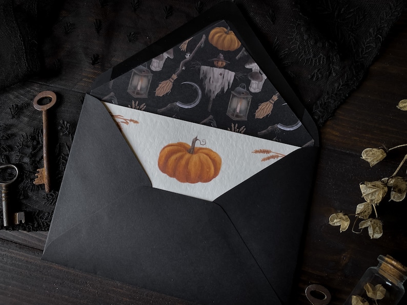 May include: A black envelope with a white card inside. The card has a drawing of a pumpkin on it. The envelope is decorated with a black and white pattern of pumpkins, lanterns, and other Halloween-themed items.