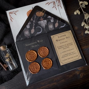 May include: A letter writing set with a black and brown color scheme. The set includes 8 sheets of printed writing paper, 4 lined envelopes, 4 handmade self-adhesive wax seals, and a lined writing guide. The paper features a spooky Halloween design with a witch, a broom, a lantern, and a crescent moon.