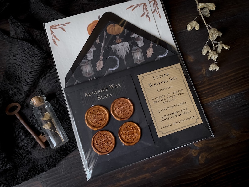 May include: A letter writing set with a black and brown color scheme. The set includes 8 sheets of printed writing paper, 4 lined envelopes, 4 handmade self-adhesive wax seals, and a lined writing guide. The paper features a spooky Halloween design with a witch, a broom, a lantern, and a crescent moon.