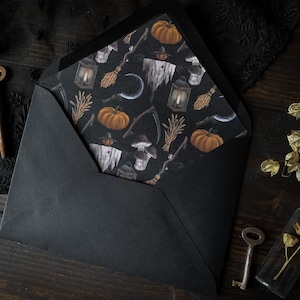 May include: A black envelope with a Halloween-themed paper insert. The insert features a repeating pattern of pumpkins, lanterns, and other spooky imagery.