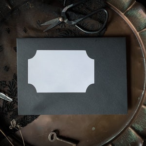 May include: A black envelope with a white, scalloped label on a vintage, copper tray. The tray has a scalloped edge and is surrounded by black lace.