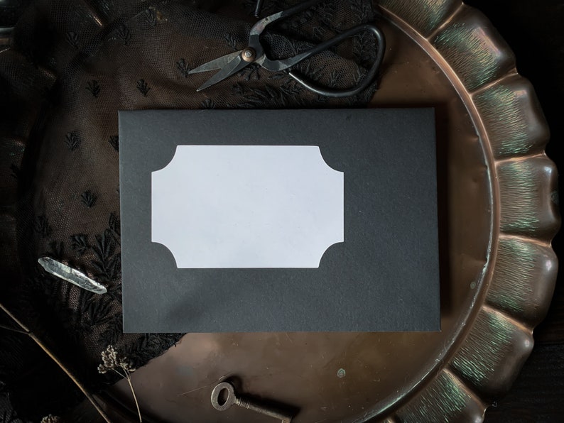 May include: A black envelope with a white, scalloped label on a vintage, copper tray. The tray has a scalloped edge and is surrounded by black lace.