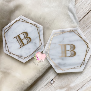 May include: Two white marble hexagon coasters with gold trim and the letter "B" in gold lettering.