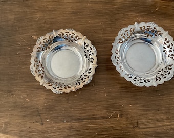 May include: Two silver-plated decorative plates with intricate cut-out designs. The plates are round and have a raised edge.
