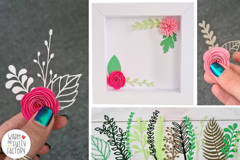 May include: A white frame with a pink paper flower and green leaves inside. There are additional pink paper flowers and green leaves on a white surface.