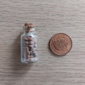 May include: A small glass bottle with a cork stopper filled with brown and white ceramic animal figurines. A copper-colored British 1 pence coin is next to the bottle.