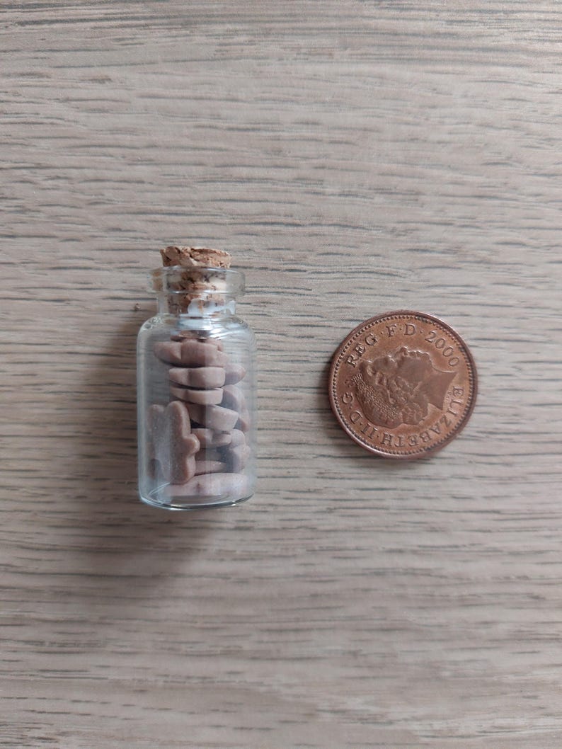 May include: A small glass bottle with a cork stopper filled with brown and white ceramic animal figurines. A copper-colored British 1 pence coin is next to the bottle.