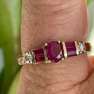 May include: A gold ring with an oval ruby centre, two rectangular rubies, and two small diamonds. The ring has a classic design with a polished gold band.