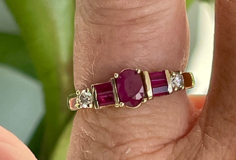 May include: A gold ring with an oval ruby centre, two rectangular rubies, and two small diamonds. The ring has a classic design with a polished gold band.