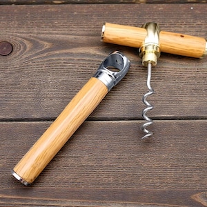 May include: Two wine bottle openers with wooden handles and metal accents are displayed on a wooden surface. One opener is open, and the other is closed. The openers are for removing corks from wine bottles.